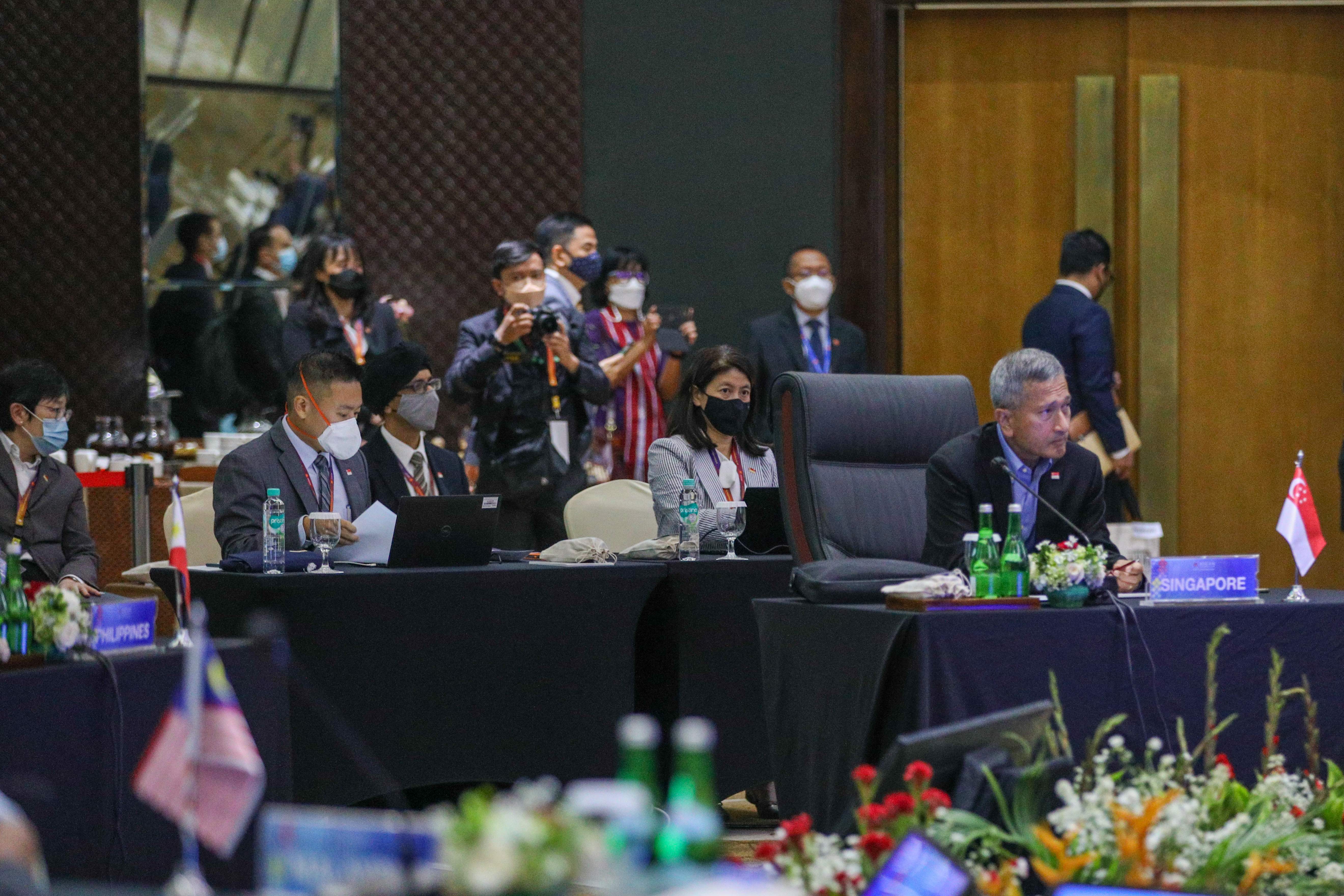People in a conference room, some wearing masks, with Singapore flag on table.